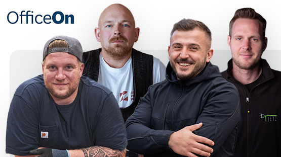 Vier Männer stehen nebeneinander, lächeln in die Kamera. Sie tragen Arbeitskleidung in verschiedenen Farben.