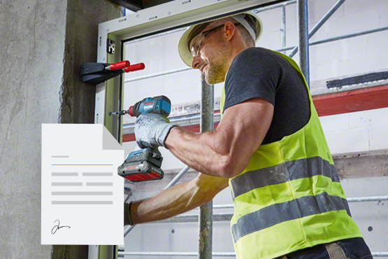 Ein Handwerker in gelber Warnweste befestigt eine Tür mit einem Akku-Schrauber.