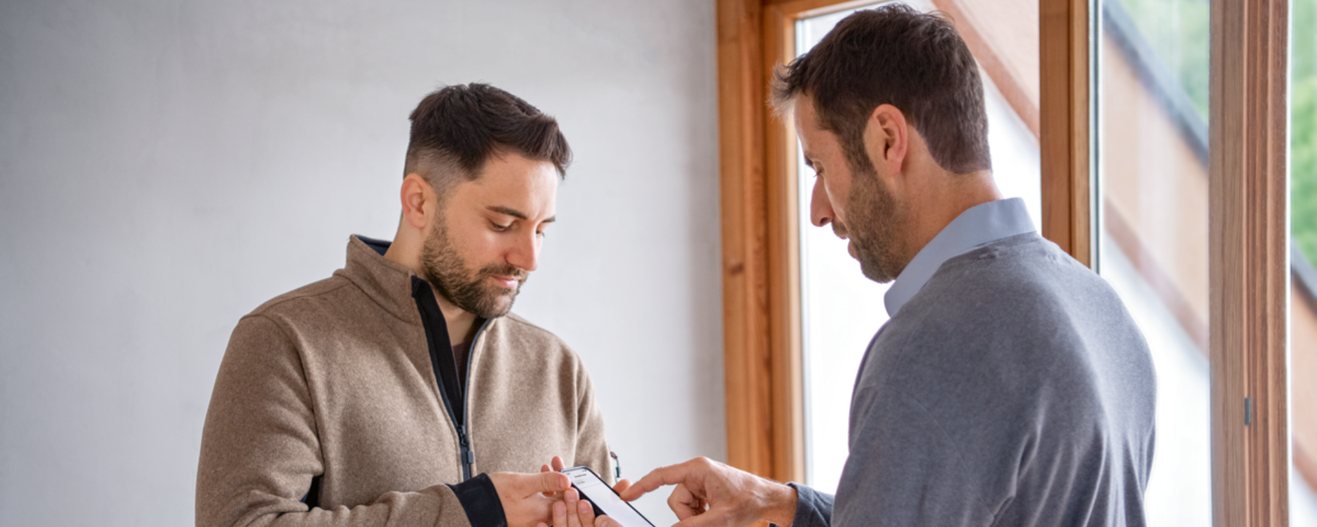 Zwei Männer betrachten gemeinsam ein Smartphone in einem hellen Raum.
