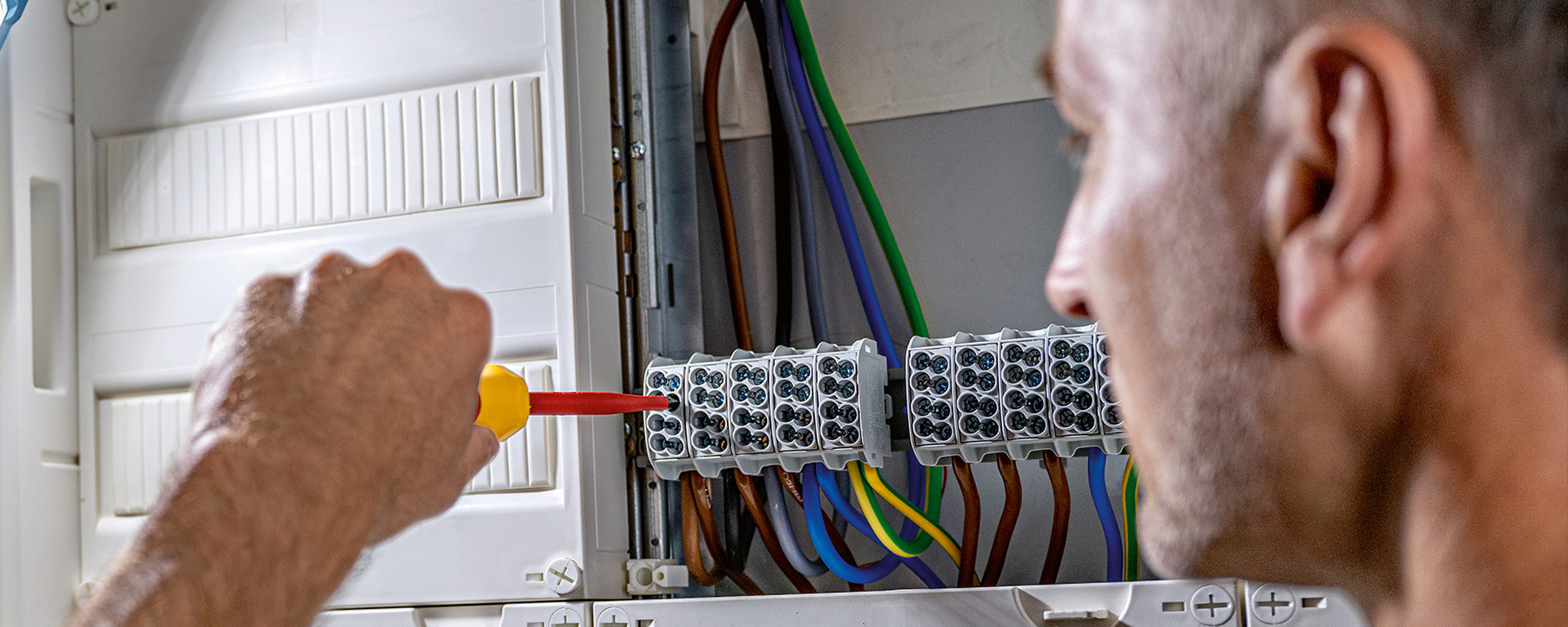 A man with a screwdriver is working on an electrical distribution.