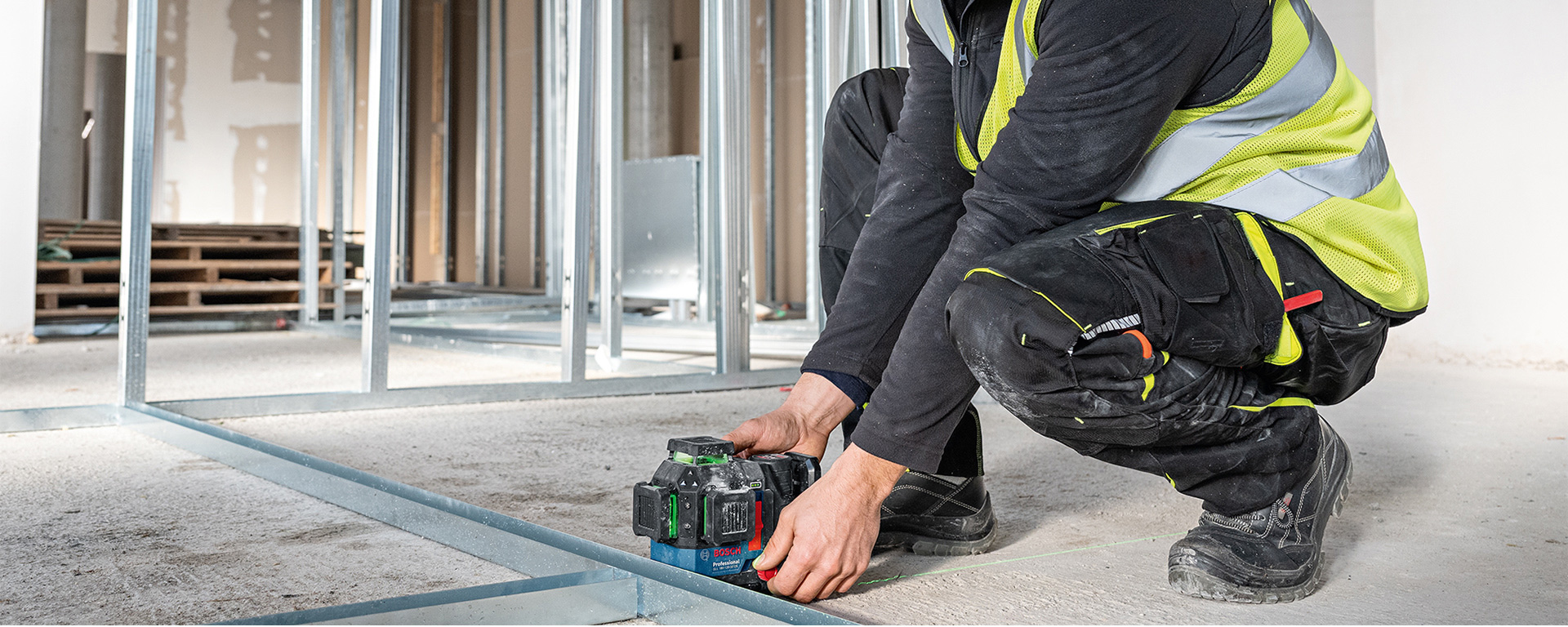 A craftsman in a yellow vest is using a Bosch Professional laser on the floor.
