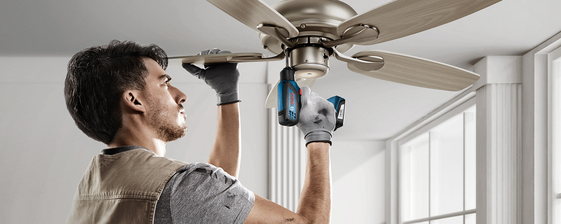 A man is installing a ceiling fan with a Bosch cordless drill.