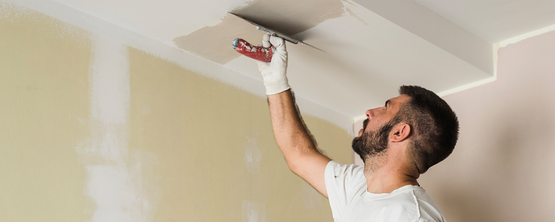 A man is painting the ceiling with a spatula in a room.