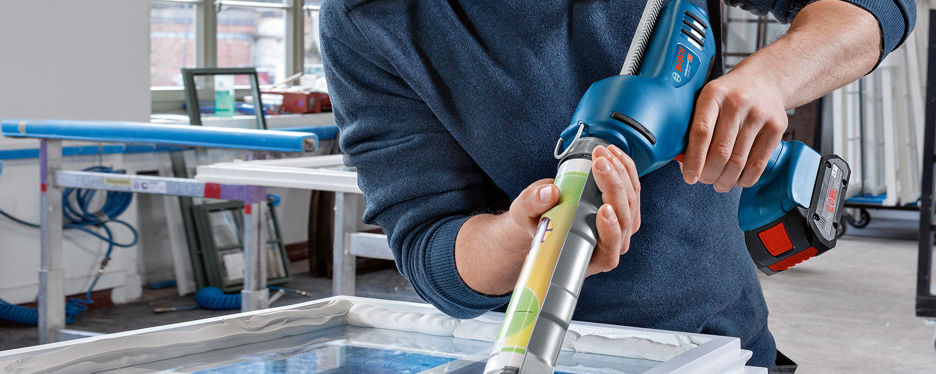 A man is using a blue Bosch Professional battery glue in a workshop.