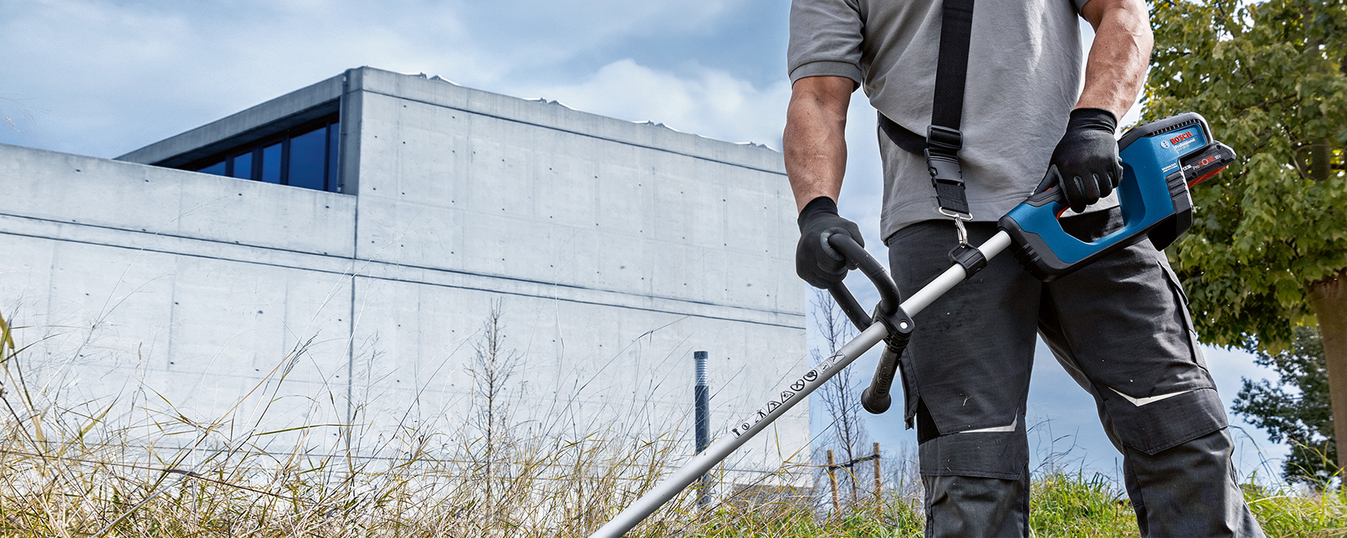 A man with Bosch Professional tools is cutting grass in front of a wall.