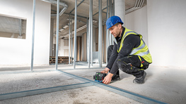 Ein Bauarbeiter mit blauer Helm nutzt eine Bosch Professional Maschine auf Beton.