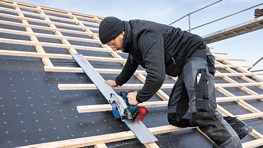 Ein Handwerker bearbeitet eine Dachlatte mit einem Bosch Werkzeug.