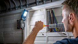 Ein Mann arbeitet mit einem Schraubendreher an einem Schaltschrank.