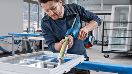 Ein Mann mit einer Akku-Silikonpistole dichtet ein Fenster ab.