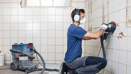Ein Handwerker in Schutzmaske schleift Fliesen mit einer Maschine.