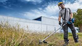 Ein Mann mäht Gras mit einem Bosch Freischneider in einem Garten.