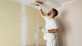 Ein Mann in weißer Kleidung streicht eine Wand mit einem Pinsel.