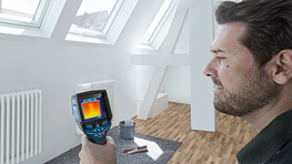 Ein Mann hält ein Wärmebildgerät in einem hellen Raum mit Dachfenstern.