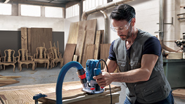 Ein Mann nutzt einen blauen Bosch Professional Fräser in einer Werkstatt.