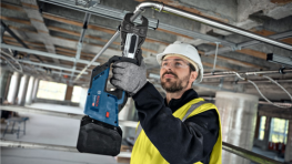 A man in safety clothing is using a blue Bosch cordless screwdriver.