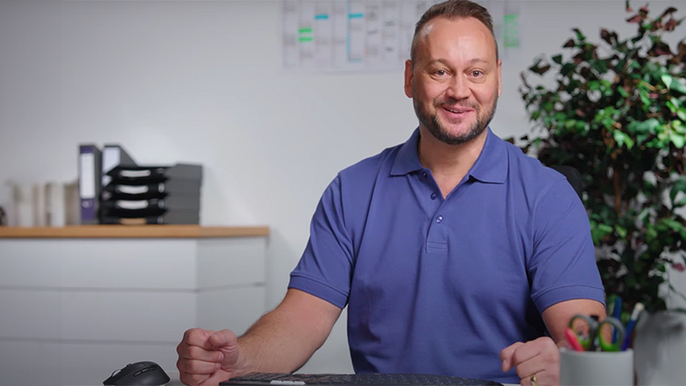 Ein Mann in blauem Shirt sitzt an einem Tisch mit Büromaterialien.